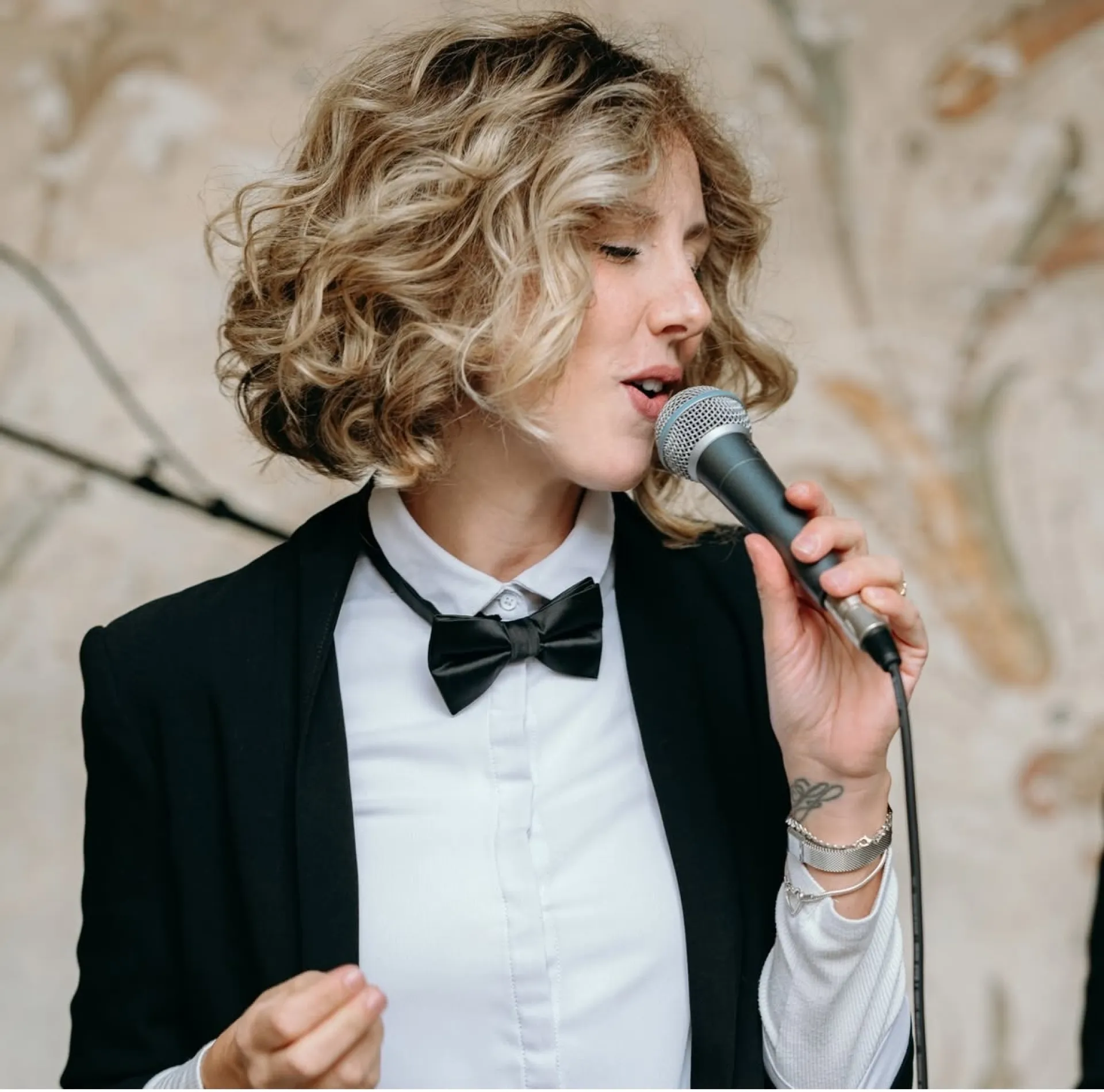 Cantante in abito formale con papillon nero che canta al microfono in una sala elegante (Victor Music)