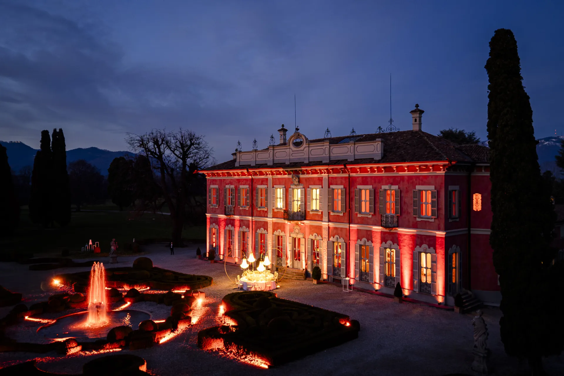 Villa e giardino all’imbrunire con illuminazione architetturale su facciata, fontana e parterre (Victor Music)
