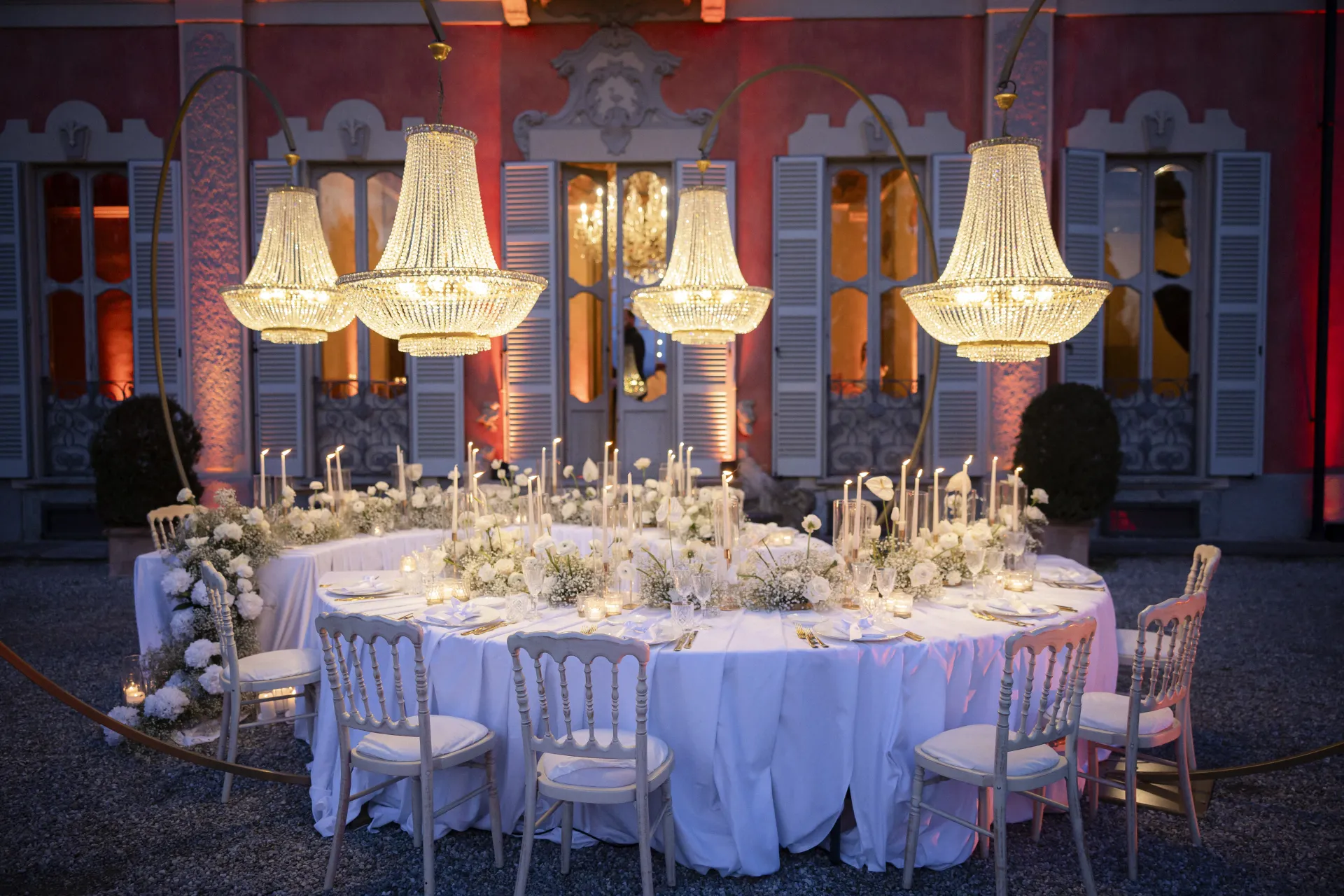 Chandelier sopra tavola rotonda imbandita davanti a villa illuminata all’aperto (Victor Music)